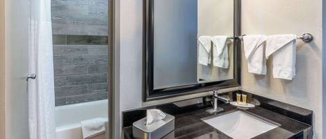 A modern bathroom with a black countertop, a white sink, a mirror, and a towel rack.