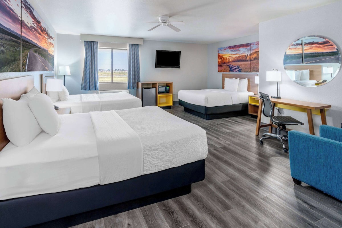 A hotel room with two beds, a desk, a chair, a TV, and a large window.