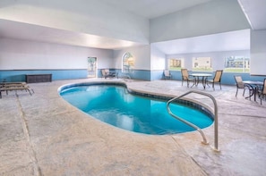 An indoor swimming pool with a curved design, surrounded by seating areas and a view of the outdoors.