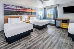 Een hotelkamer met twee bedden, een bureau, een televisie en een raam met gordijnen.