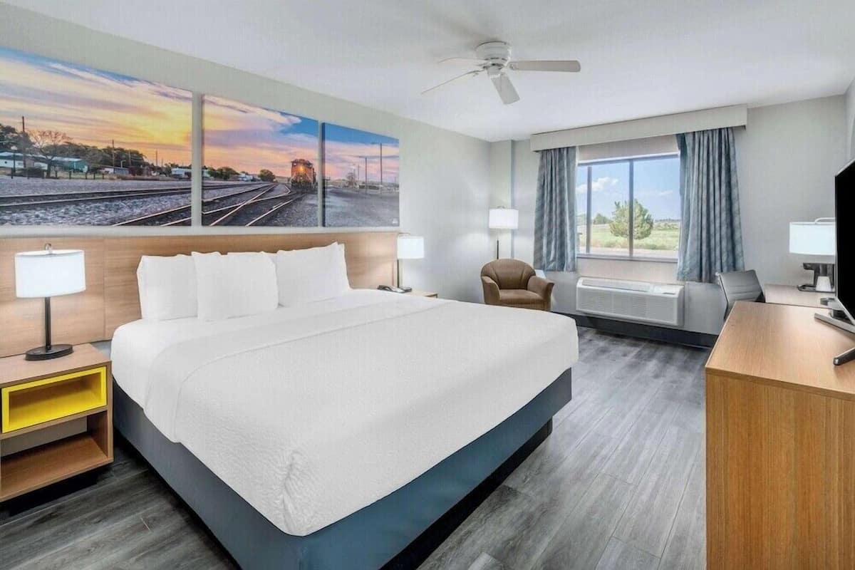 A hotel room with a large bed, a desk, a chair, a television, and a window with curtains.