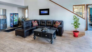 A living room with a sectional sofa, a coffee table, a red potted plant, and a wall-mounted TV. - Days Inn by Wyndham Lamar (Lamar)