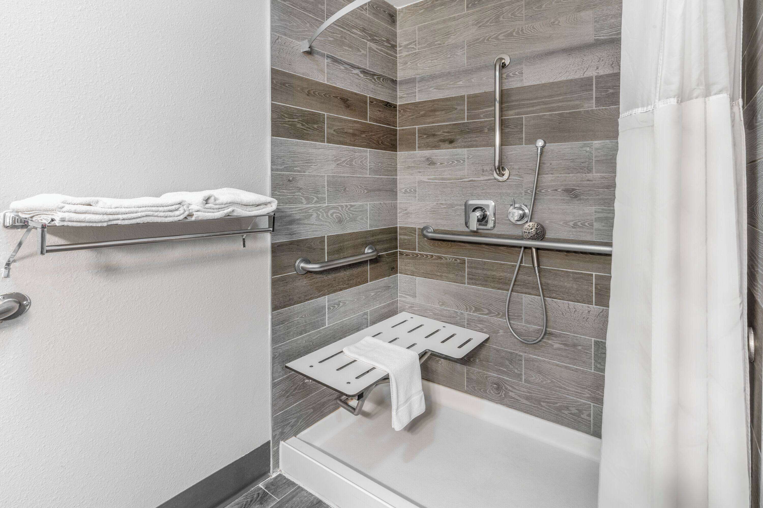 A modern bathroom with a shower, grab bars, and a towel rack.