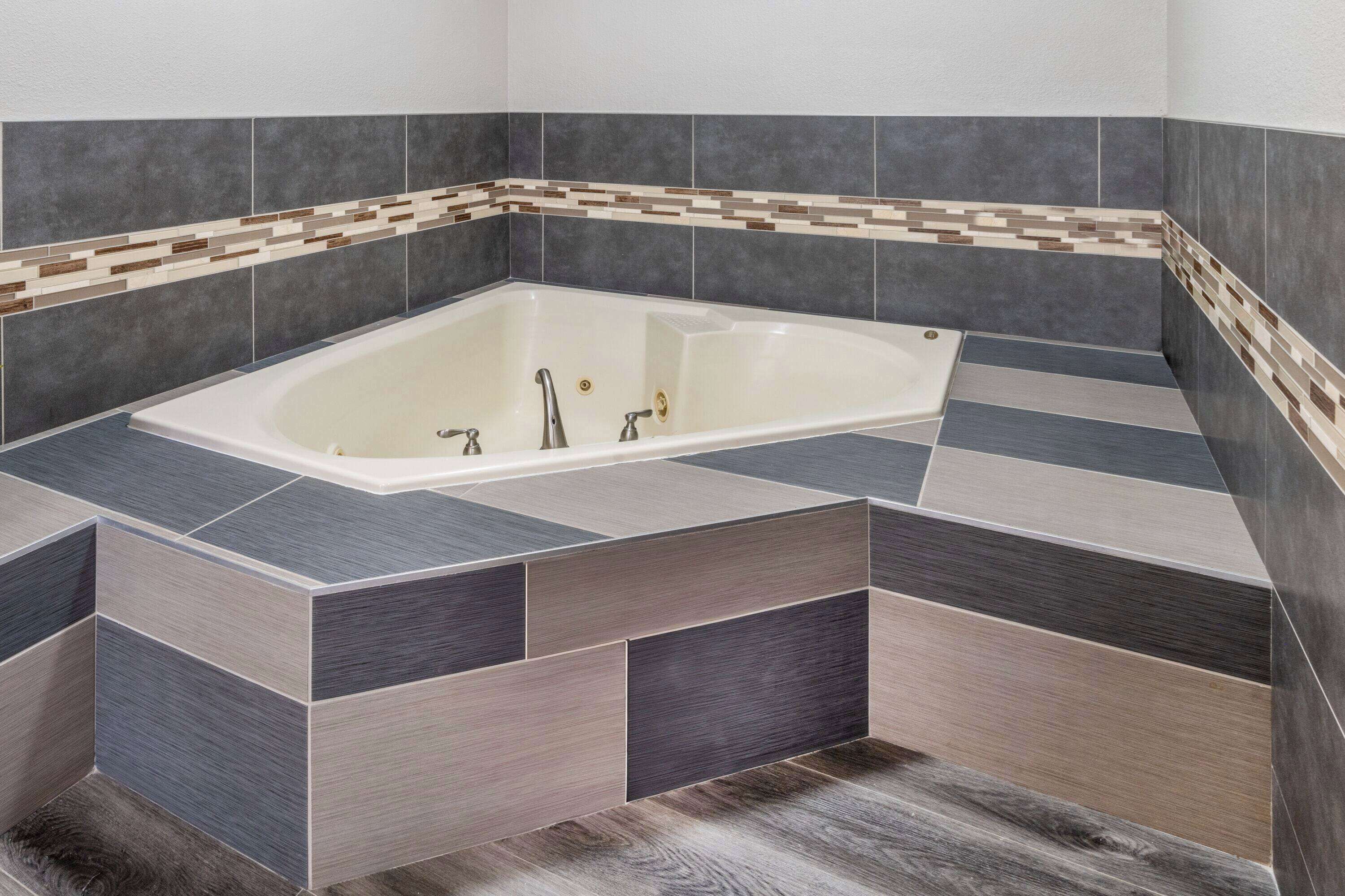 Un baño moderno con una bañera independiente, paredes con azulejos y piso de madera.