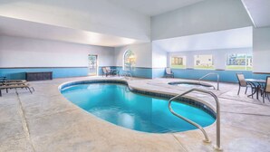 A large indoor swimming pool with a curved design, surrounded by lounge chairs and tables, and large windows offering views of the outdoors. - Days Inn by Wyndham Lamar (Lamar)