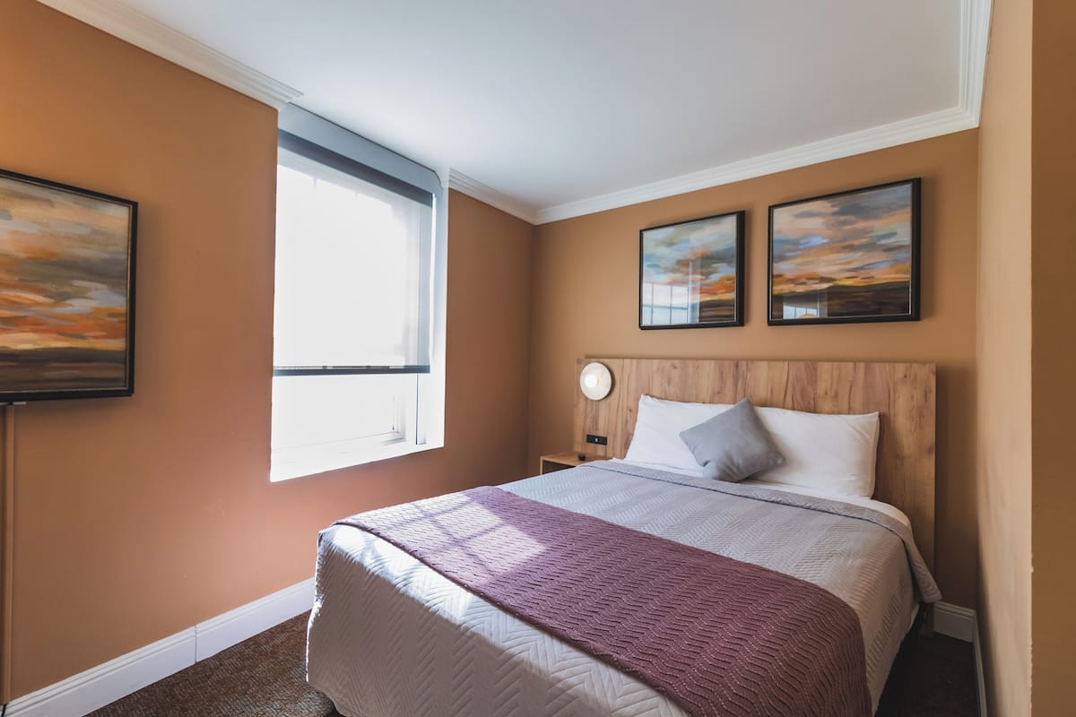 A hotel room with a large bed, a window, and two wall-mounted paintings.