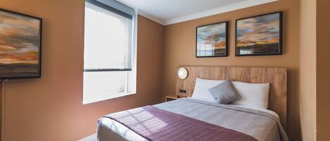 Una camera d'albergo con un letto grande, una finestra e due quadri appesi alle pareti.