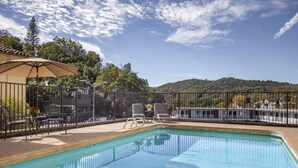 A rectangular swimming pool with a clear blue water surface, surrounded by a black metal fence. There are lounge chairs and a table with a potted plant nearby. - Historic Sonora Inn (Sonora)