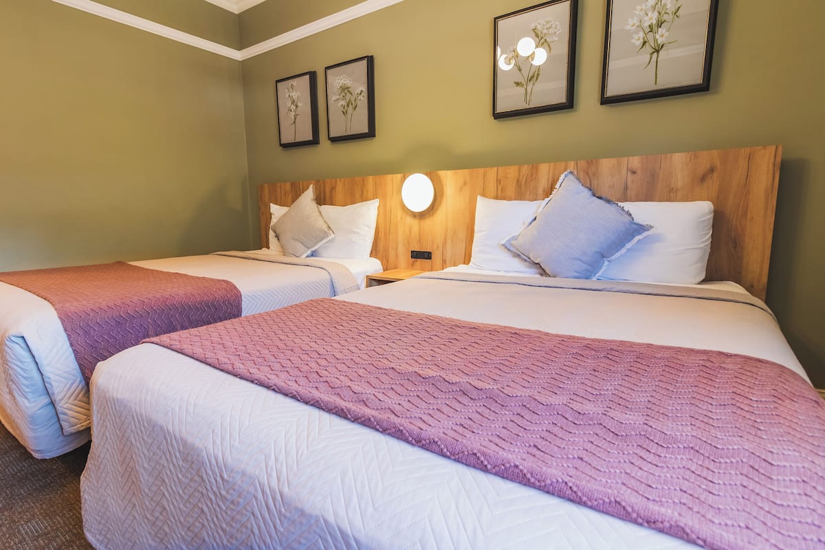 A hotel room with two beds, each with a wooden headboard and white bedding. There are three framed floral pictures on the wall.