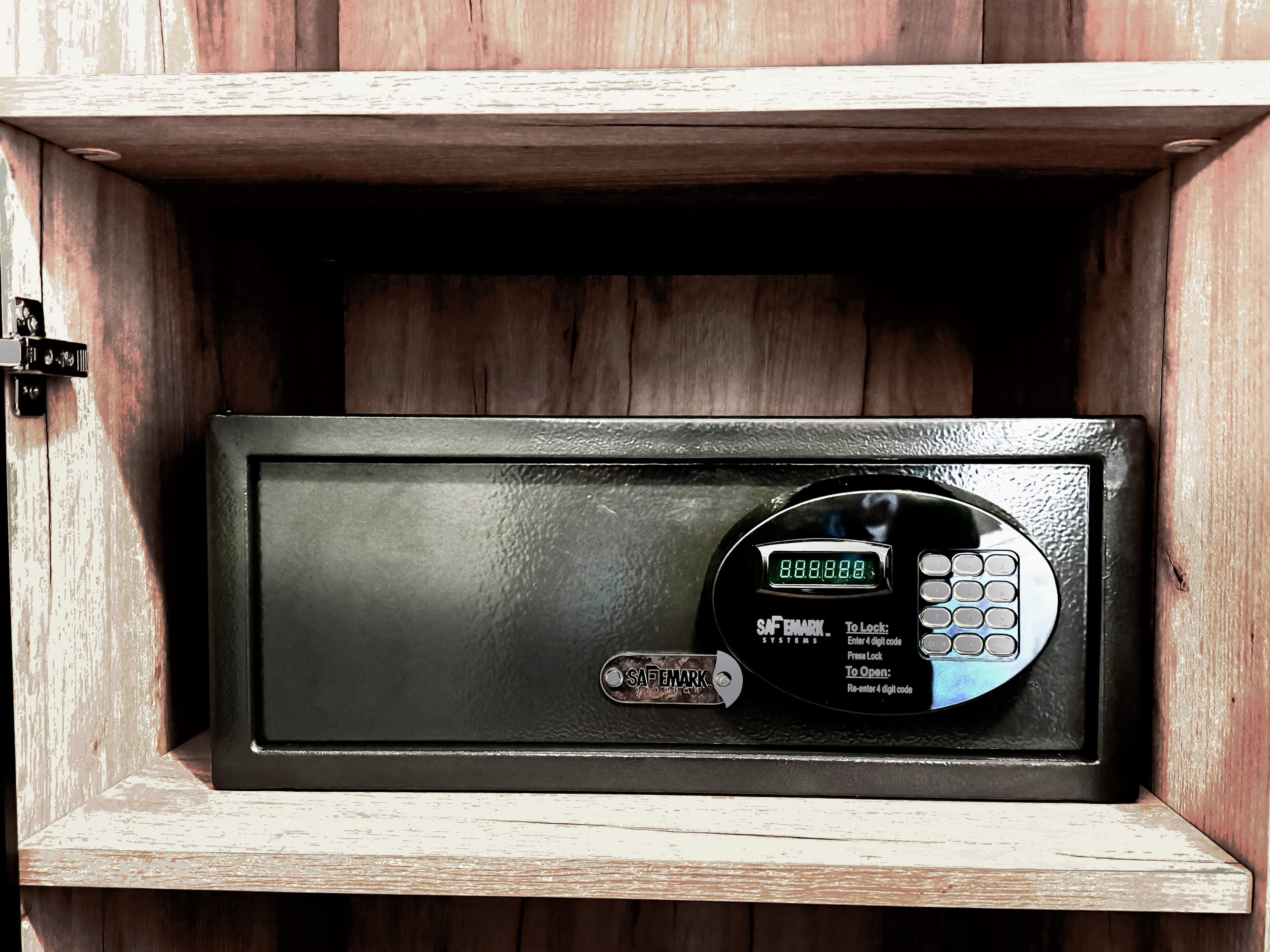 A black safe with a digital keypad, labeled "SAFEMARK SYSTEMS," inside a wooden cabinet.