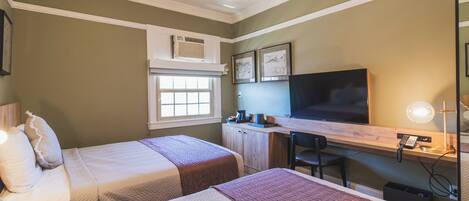 A bedroom with two beds, a desk, a television, and a window.