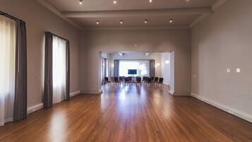 Una habitación amplia con suelo de madera, ventanas grandes con cortinas y una mesa de conferencias con sillas.