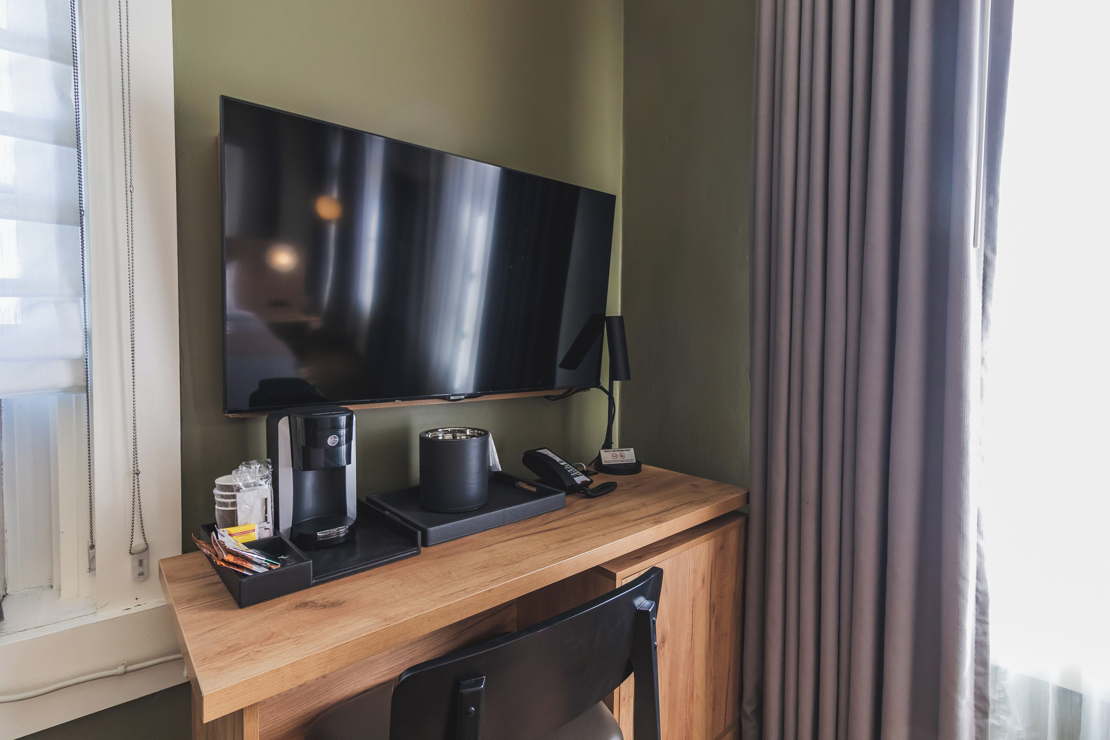 Et hotelværelse med et træskrivebord, et fladskærms-TV, kaffemaskine, telefon og lampe.