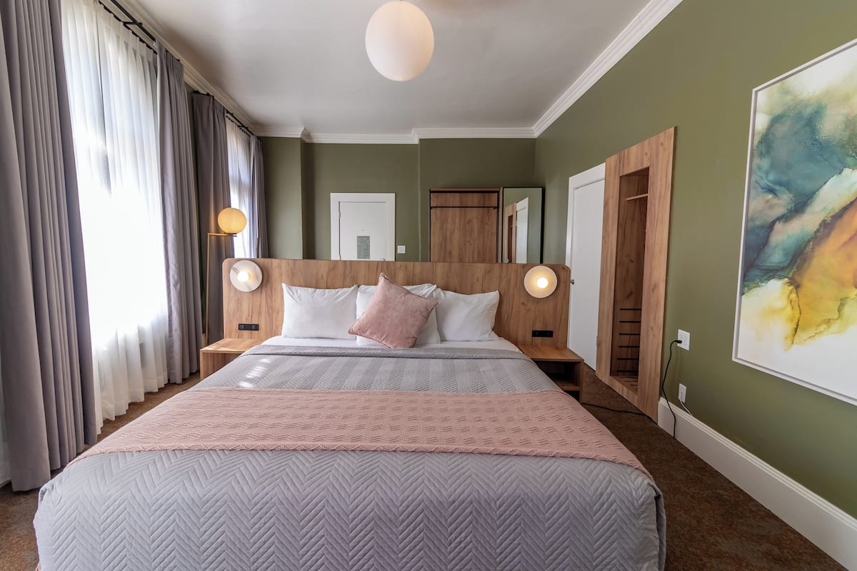 A bedroom with a large bed, wooden headboard, two bedside lamps, and a large abstract painting on the wall.