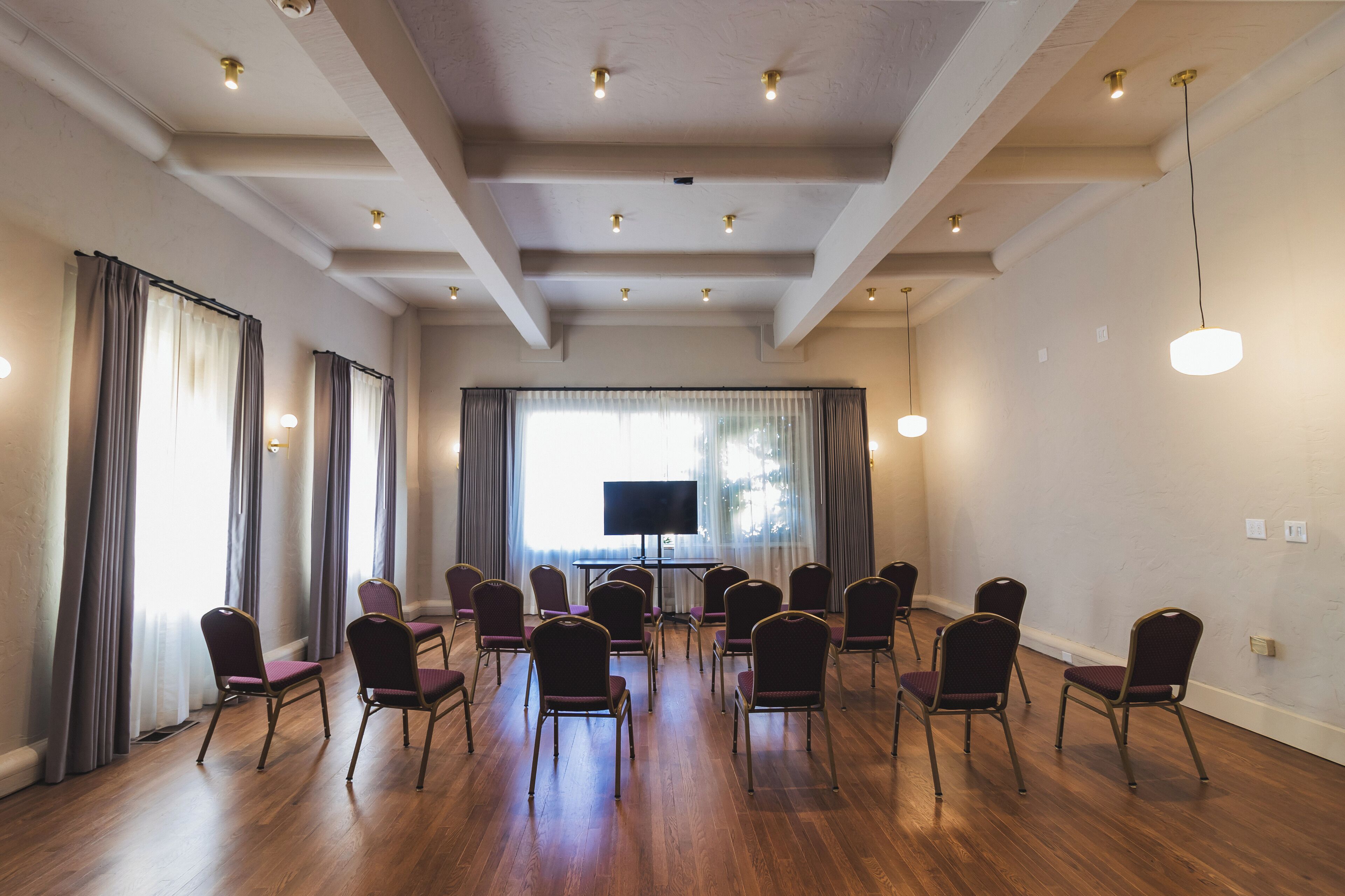 Una sala de conferencias con pisos de madera, un televisor de pantalla plana grande y filas de sillas moradas.