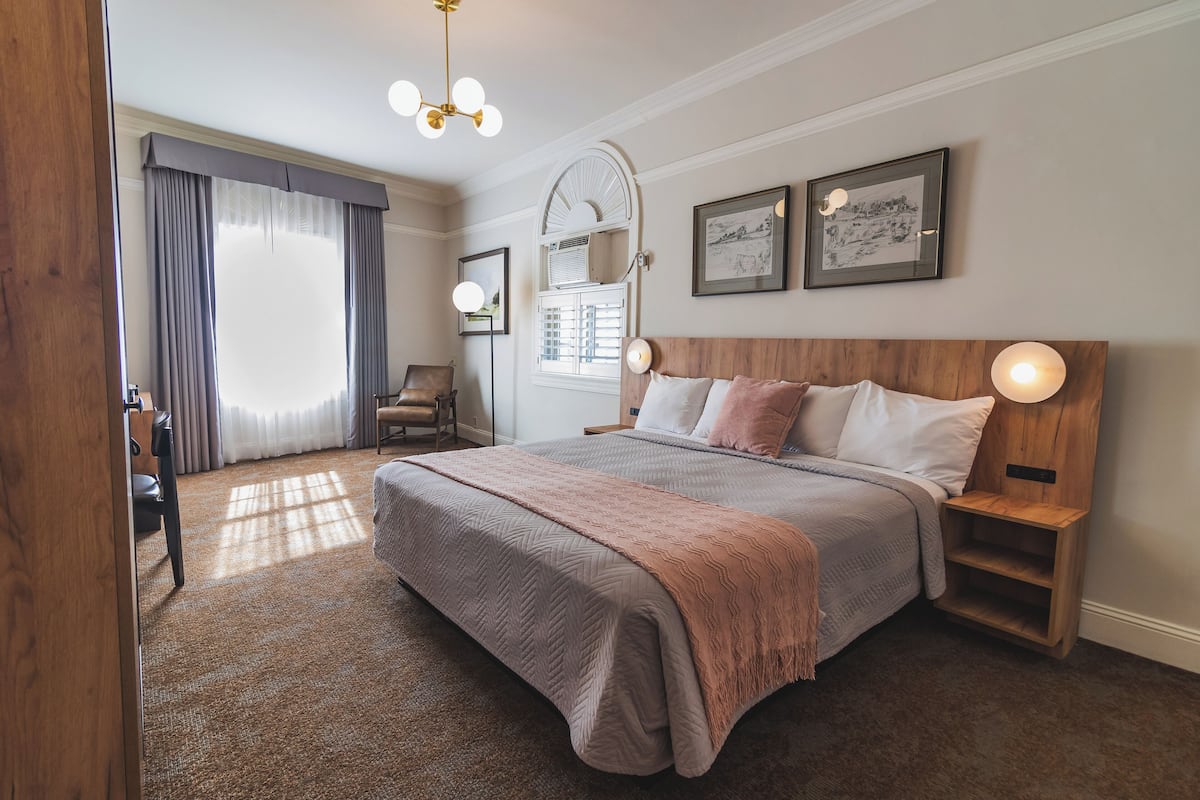 A bedroom with a large bed, wooden headboard, bedside lamps, and a window with curtains.
