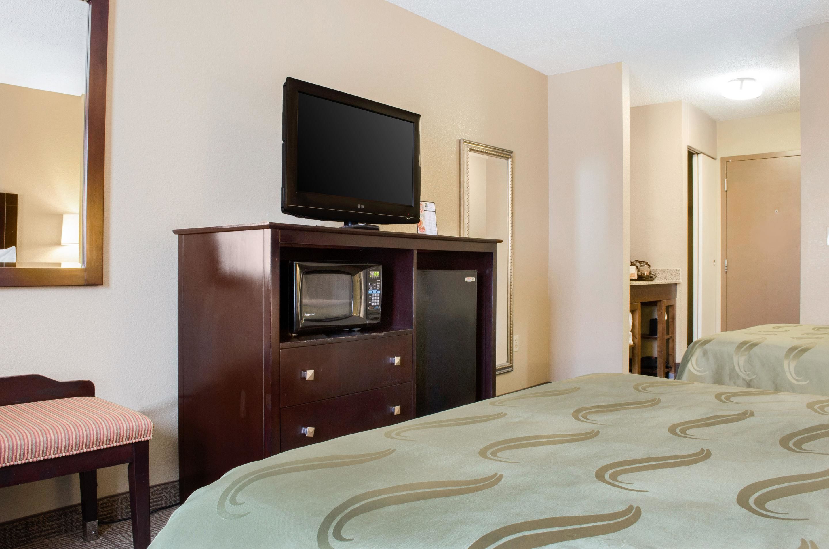 A hotel room with a bed, a television on a wooden cabinet, a microwave, and a small table with a chair.