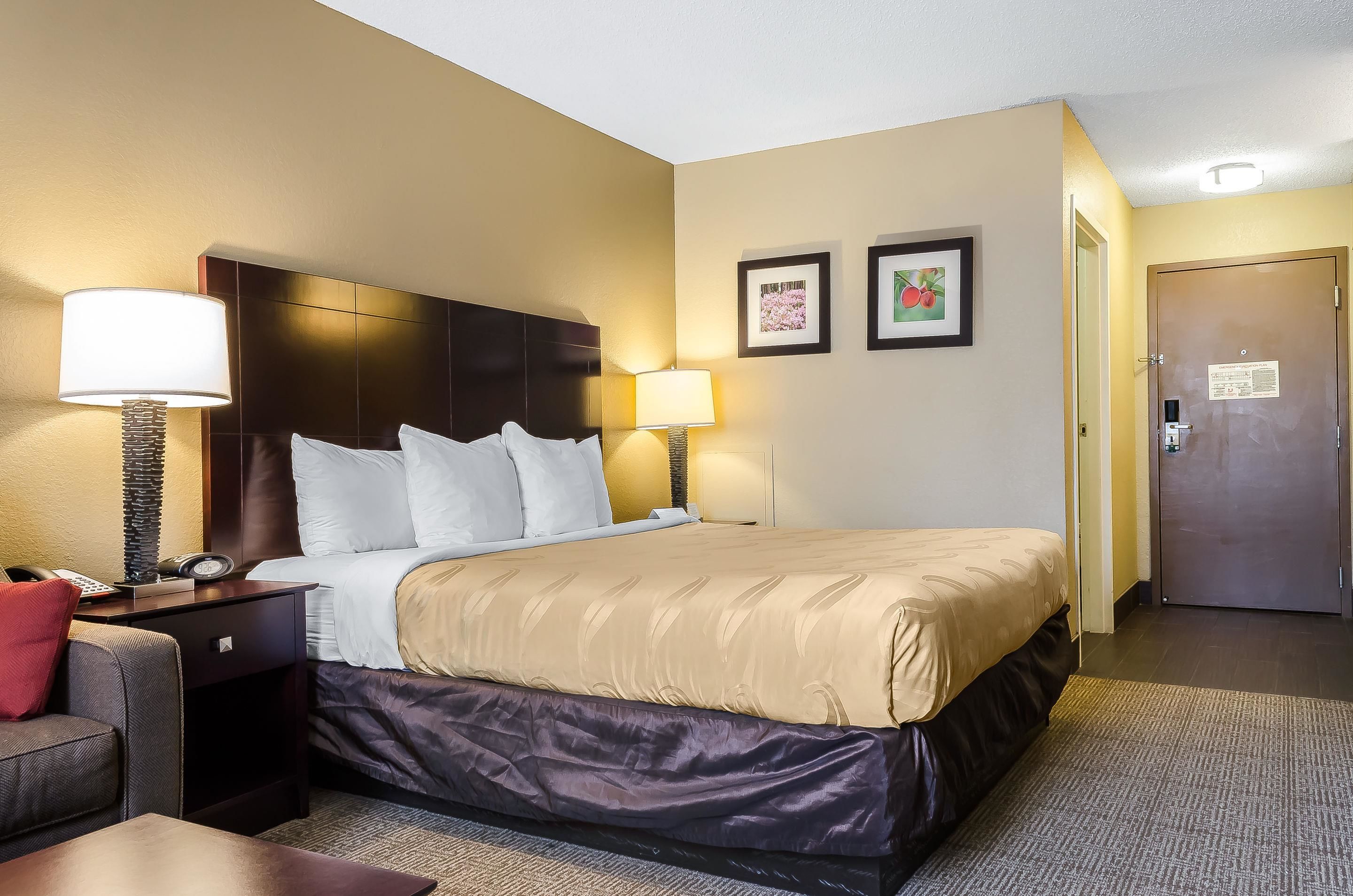 Una habitación de hotel con una cama, dos lámparas de noche, una mesita de noche, un escritorio con teléfono y una puerta.