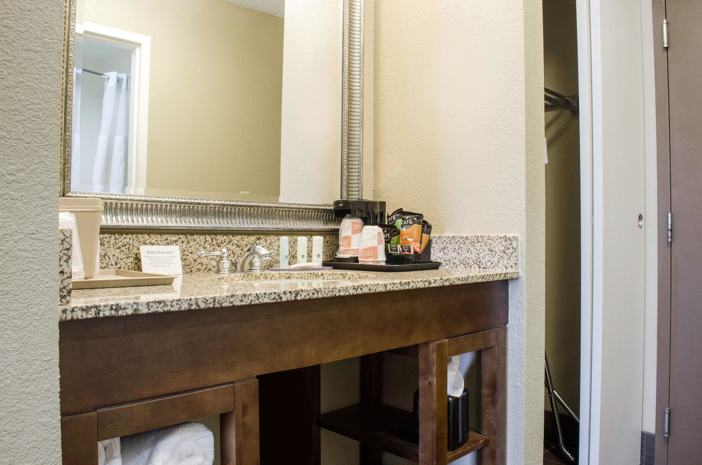 A bathroom with a granite countertop, a mirror, a towel rack, and a coffee maker.