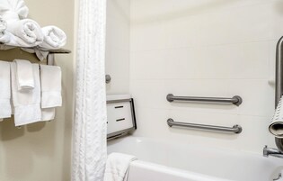 Un baño con una bañera, dos barras de apoyo y un toallero con toallas enrolladas.