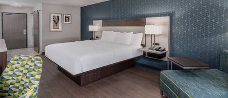 A hotel room with a large bed, two bedside tables, a desk, a chair, and a sofa.