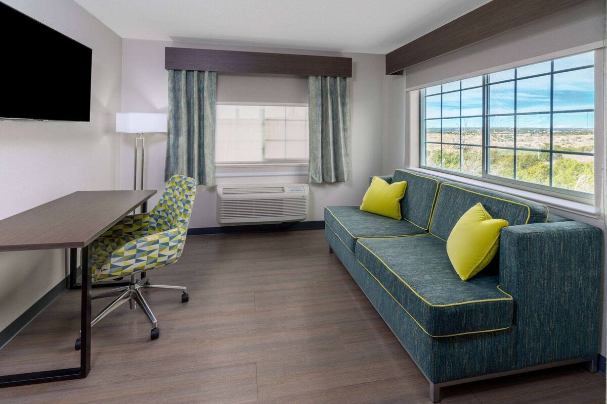 Een hotelkamer met een bureau, stoel, bank en groot raam met uitzicht.