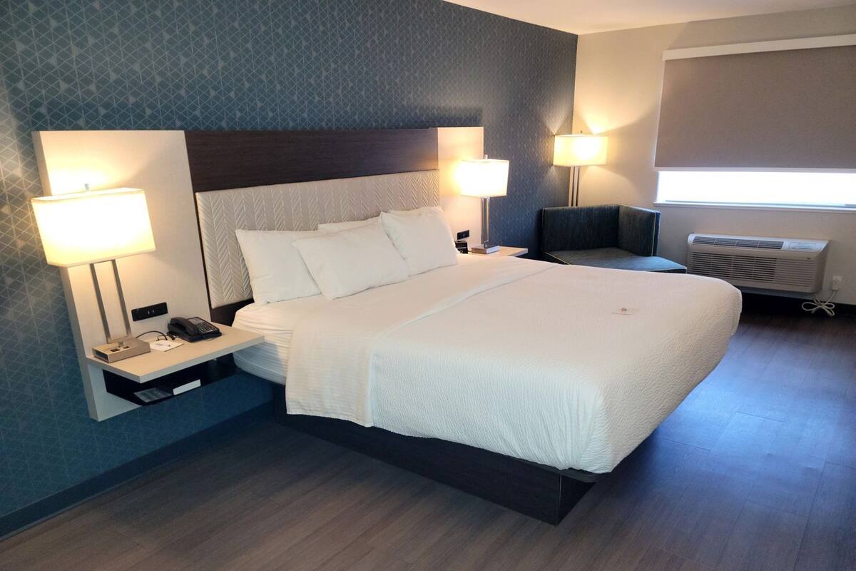 Een hotelkamer met een bed, bedlampen, een telefoon, een nachtkastje en een raam met jaloezieën.