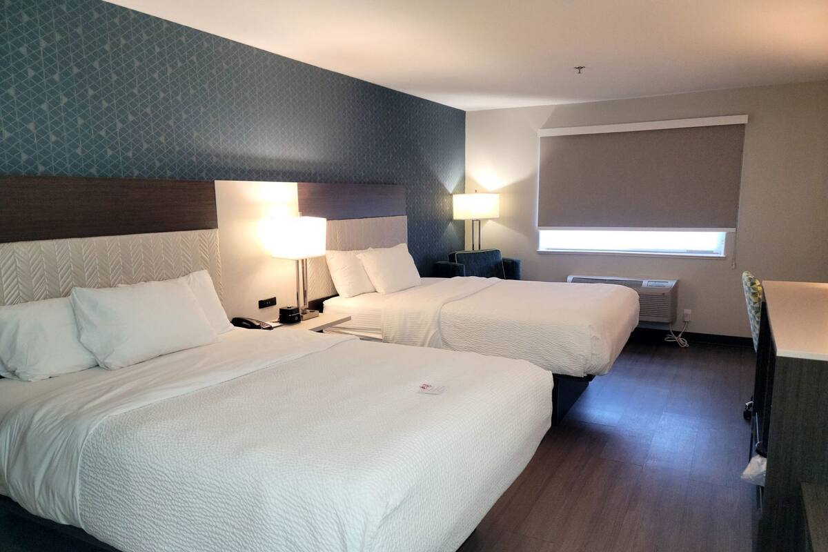 Een hotelkamer met twee bedden, een nachtkastje met lamp, een bureau met stoel, een raam met zonwering en een radiator.