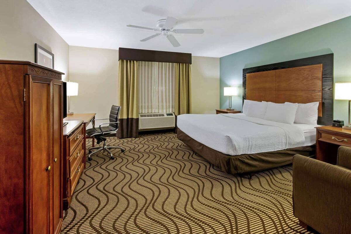 Een hotelkamer met een bed, bureau, stoel en een plafondventilator.