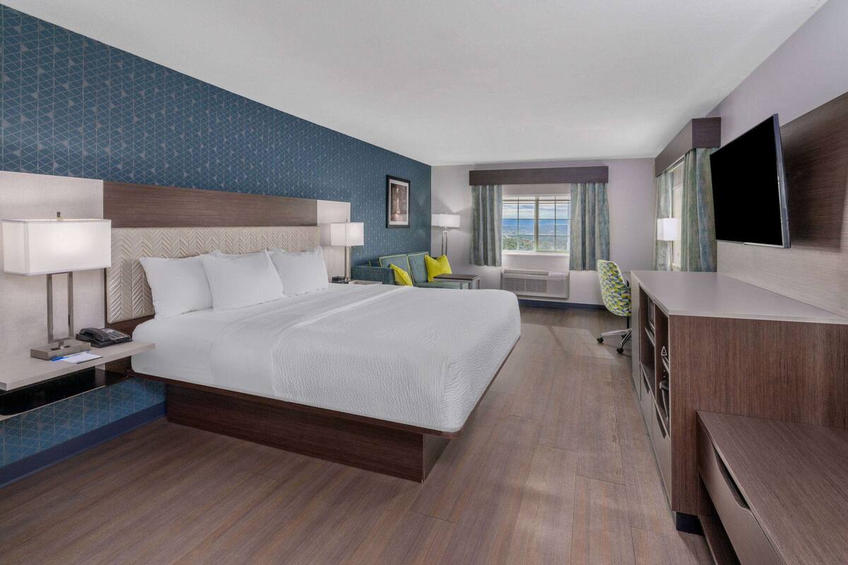 Een hotelkamer met een groot bed, nachtkastjes, een bureau, een stoel, een televisie en een raam met gordijnen.