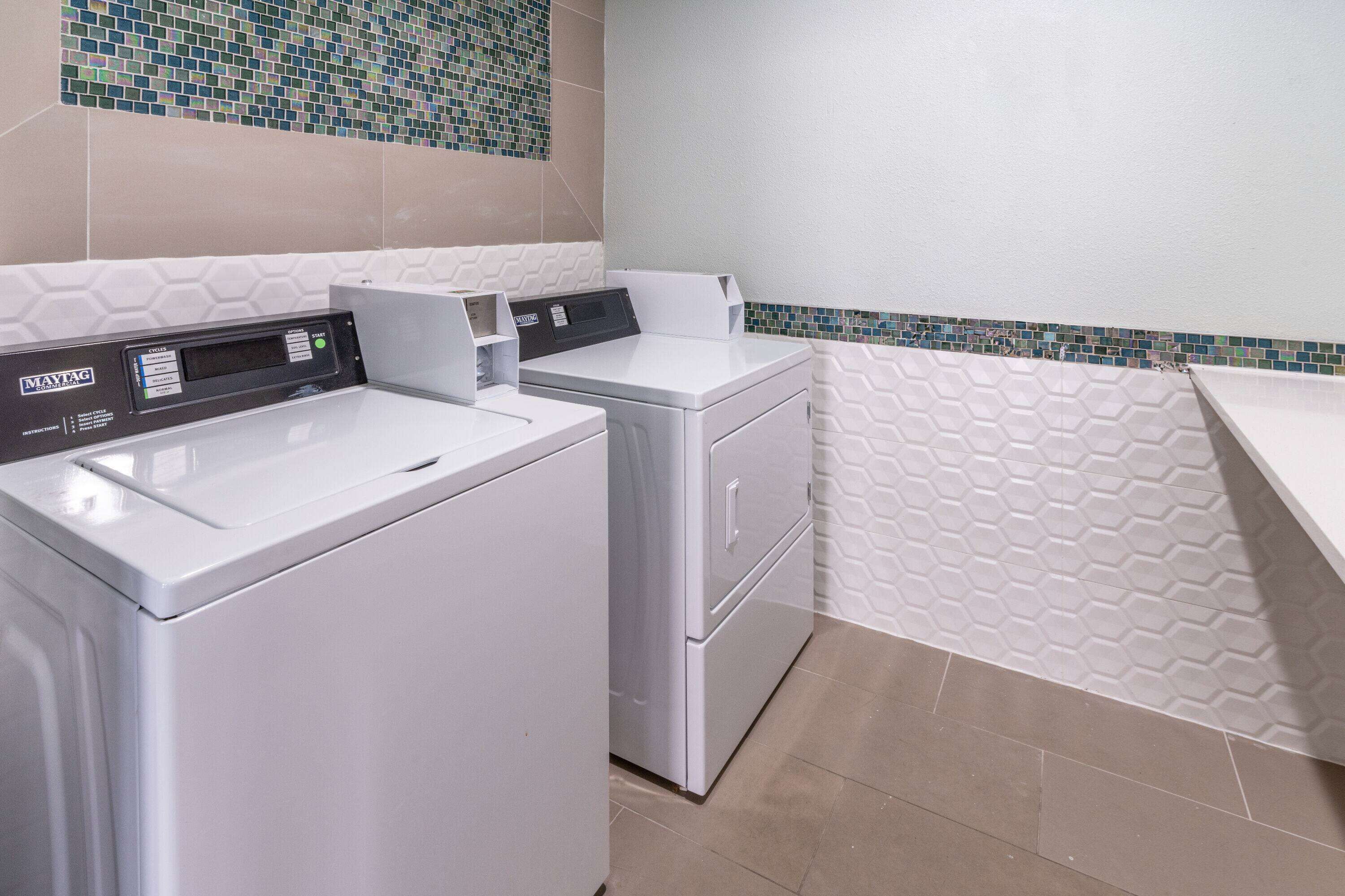 A laundry room with two white washing machines, a control panel, and a tiled backsplash.