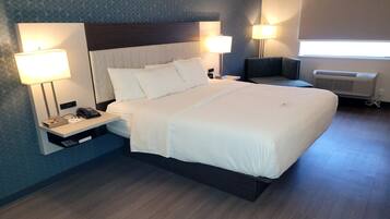 A hotel room with a large bed, two bedside tables with lamps, a bedside phone, and a wall-mounted air conditioner.
