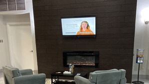 En modern entréhall med en öppen spis, två grå fåtöljer, ett svart soffbord och en platt-TV som är monterad på en mörk tegelvägg.