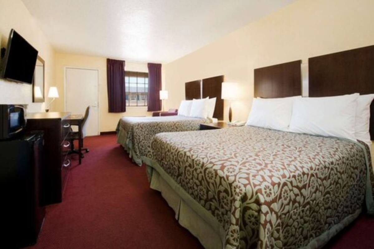 Habitación de hotel con dos camas, un escritorio, televisión y ventana con cortinas.