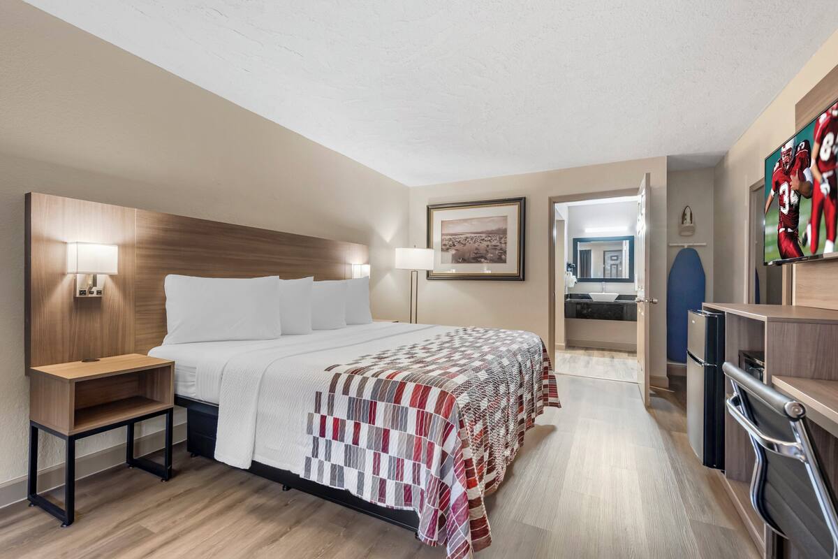 A hotel room with a large bed, bedside tables, a desk, a TV, and a kitchenette.