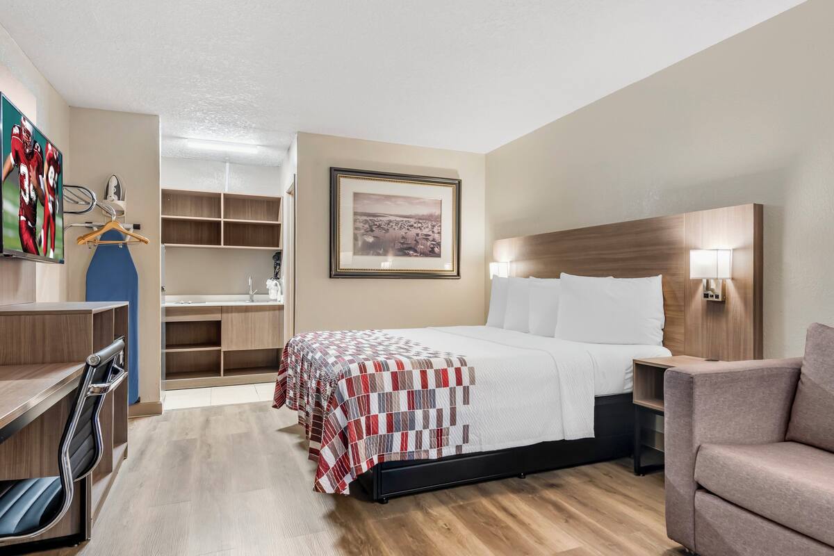 A hotel room with a bed, a desk, a chair, a wardrobe, and a framed picture on the wall.
