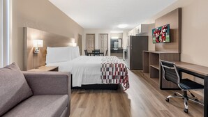 Habitación de hotel con cama, escritorio, silla, televisión y kitchenette.