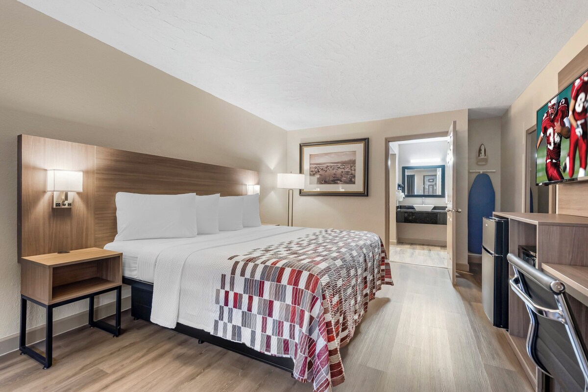 A hotel room with a large bed, bedside tables, a desk, a TV, and a kitchenette.
