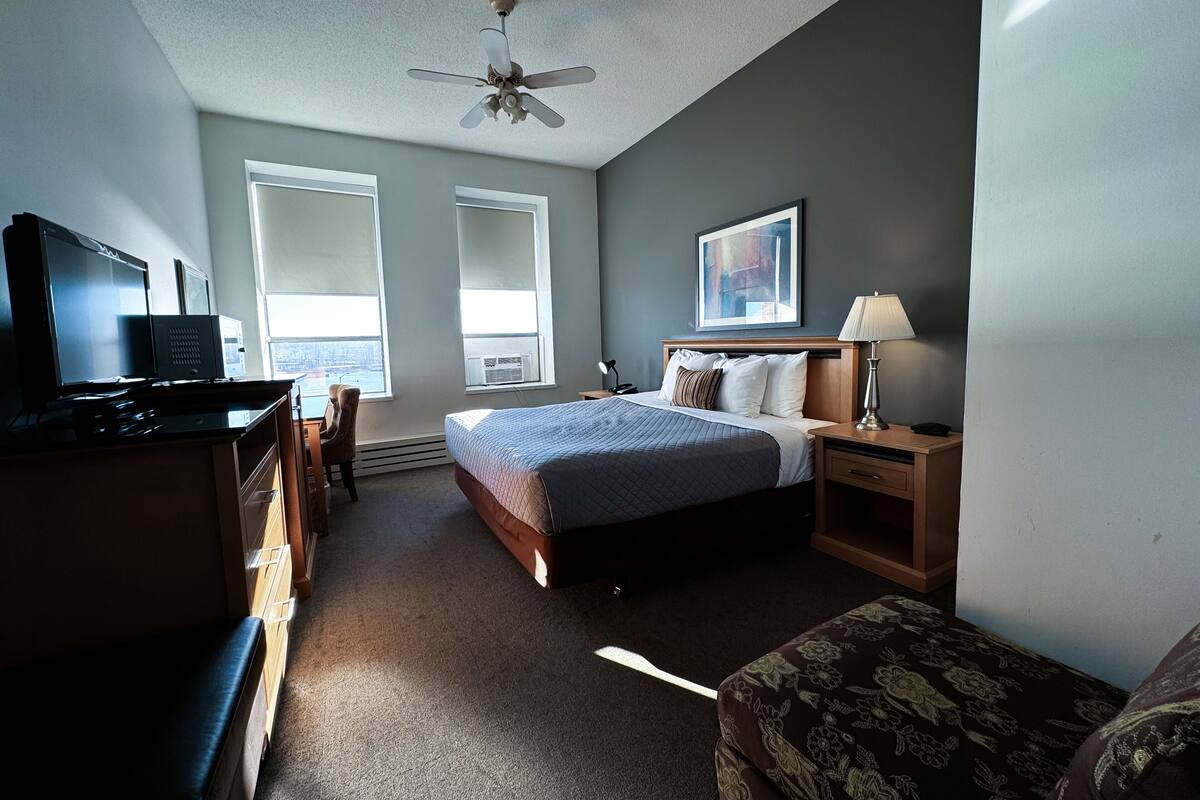A hotel room with a bed, desk, chair, television, and a ceiling fan.
