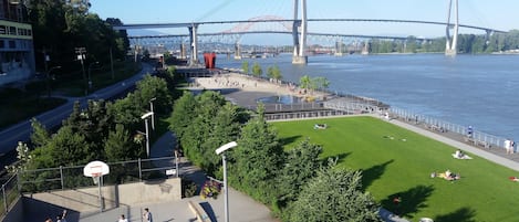 A park with a basketball court, a grassy area with people relaxing, and a bridge in the background.