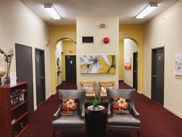 A hotel lobby with a reception desk, two armchairs with floral cushions, a globe on the desk, and a large abstract painting on the wall.