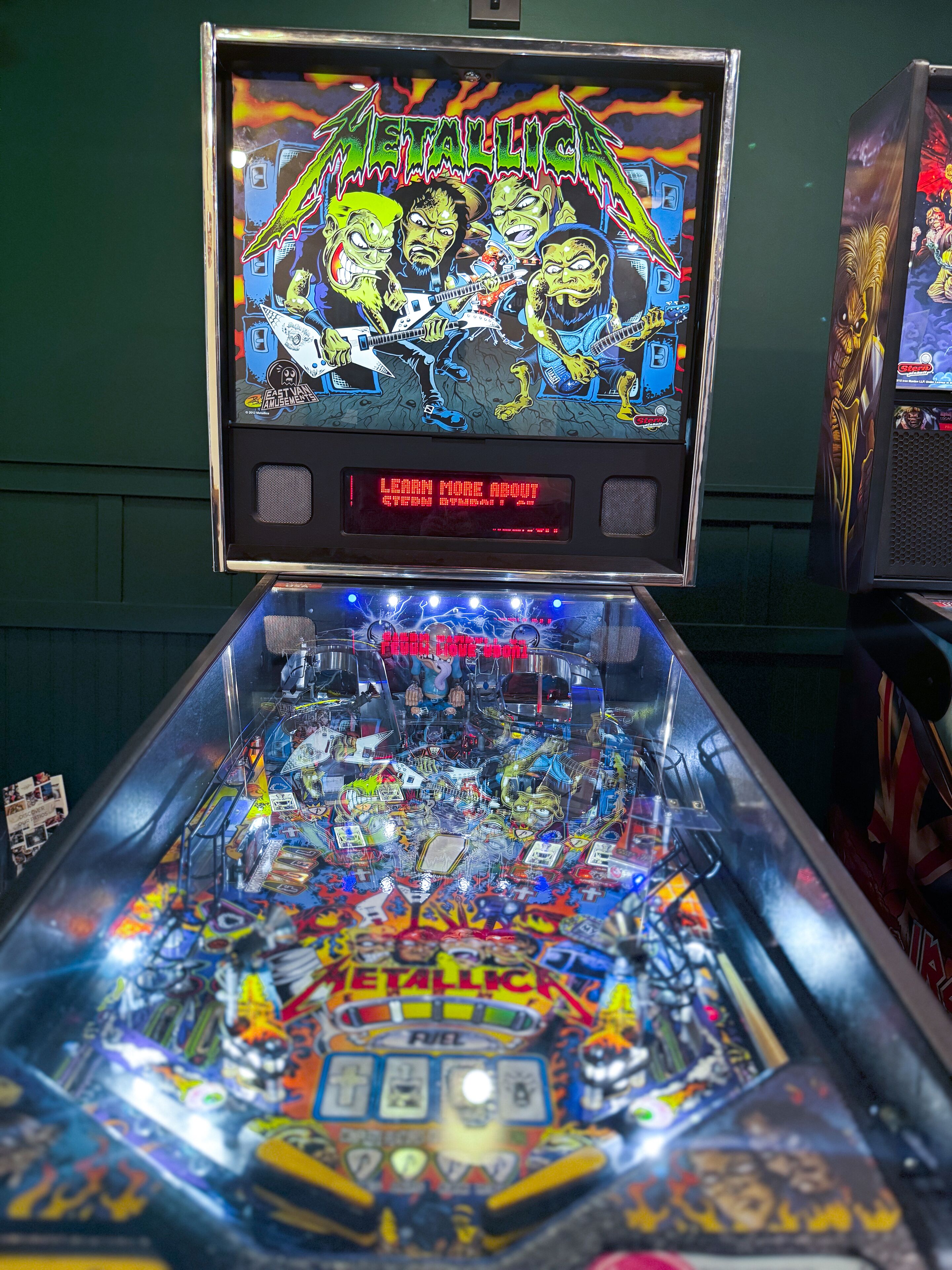 Una máquina de pinball con temática de Metallica, que presenta una pantalla grande mostrando el logo y personajes de la banda.