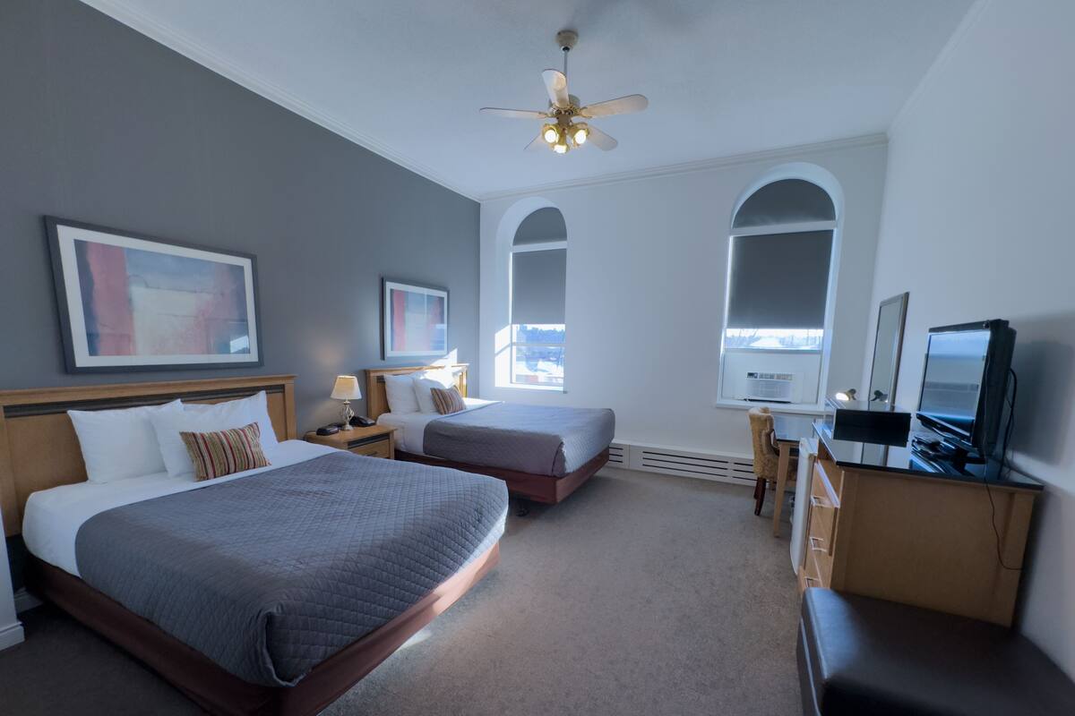 A hotel room with two beds, a desk, a television, and a ceiling fan.