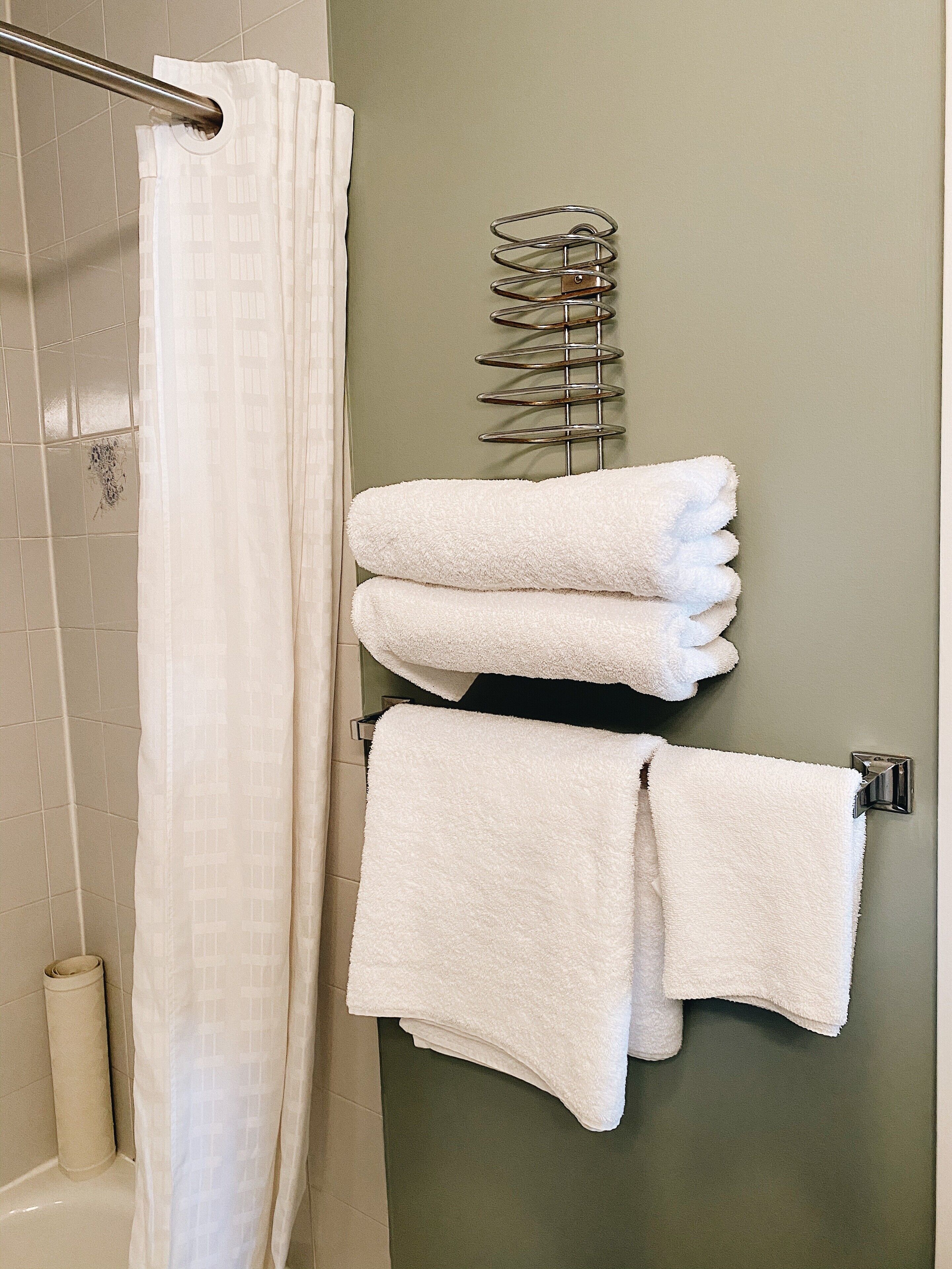 Un baño con cortina de ducha, toallero con toallas dobladas y pared de azulejos.