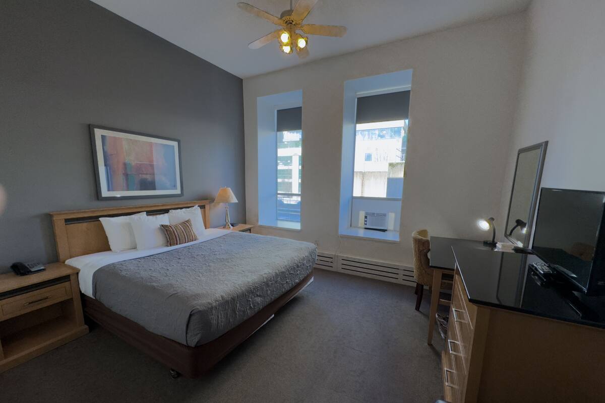 A bedroom with a bed, bedside table, lamp, dresser, mirror, and a ceiling fan.
