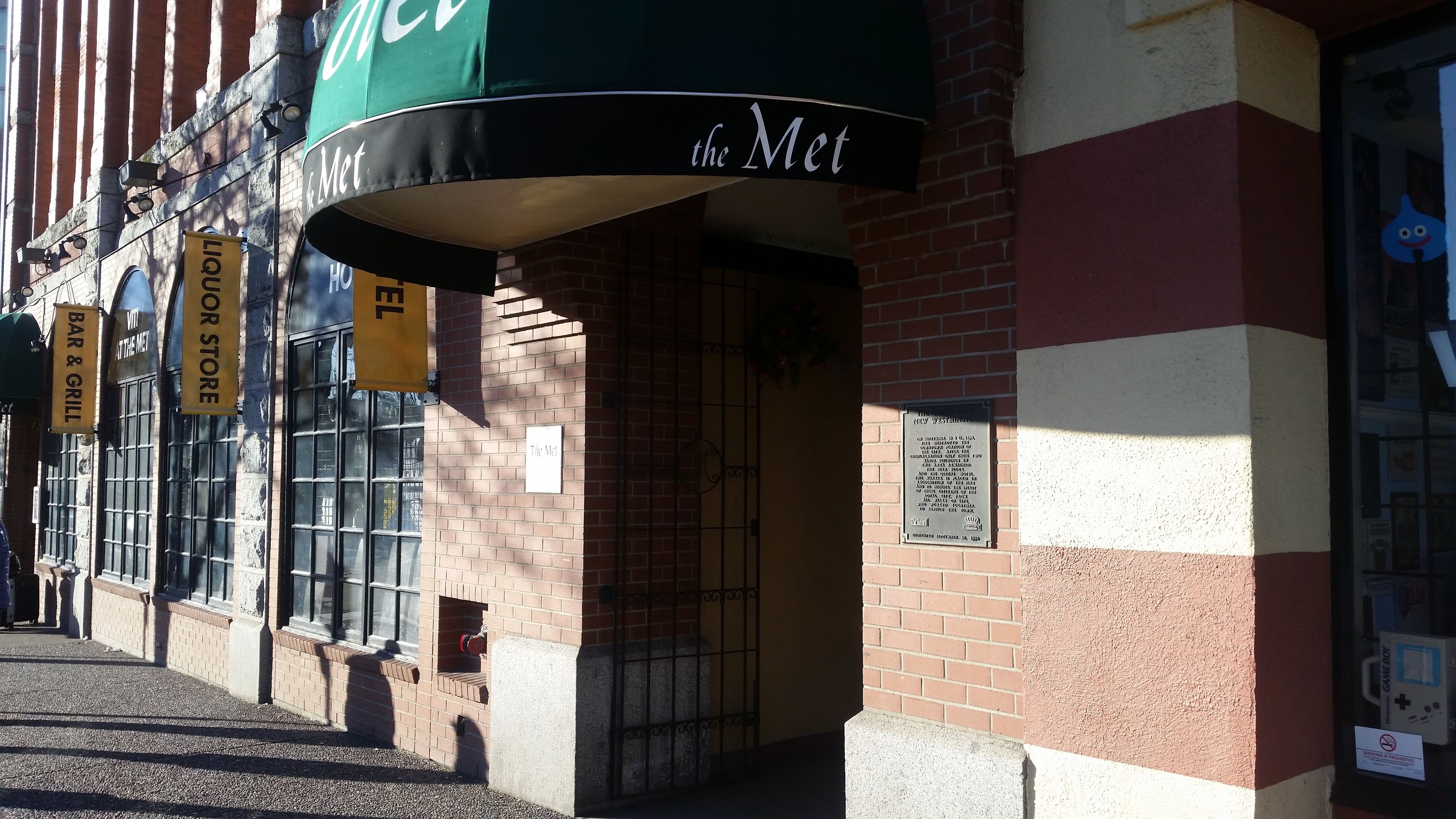 Un edificio de ladrillo con un toldo verde que dice "the Met" y un letrero amarillo para una licorería.