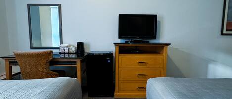 Una habitación de hotel con dos camas, un escritorio con computadora, televisor y un refrigerador pequeño.