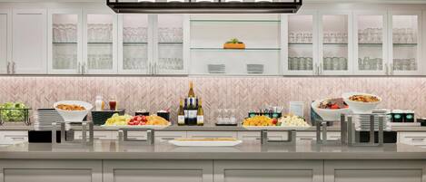 Une cuisine moderne avec des meubles blancs, une étagère vitrée et divers produits alimentaires.