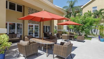 Un patio al aire libre con muebles de mimbre, sombrillas rojas y plantas en macetas.