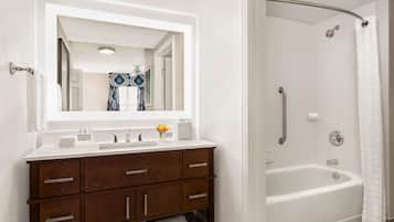 Une salle de bain avec un meuble-lavabo blanc, un grand miroir, une baignoire et un rideau de douche.